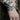 A close-up of a person's tattooed wrist and hand wearing sterling silver charm chain bracelets with charms, including a bat, sun, and pigeon designs, against a blurred outdoor background.