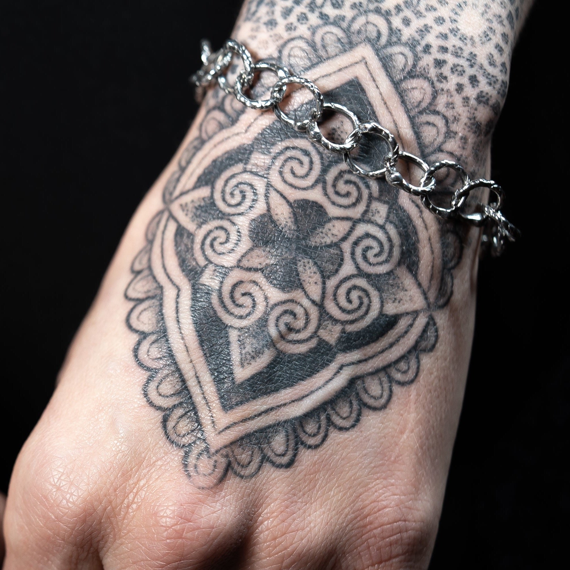 Handmade snake-link bracelet on a tattooed wrist with a black background
