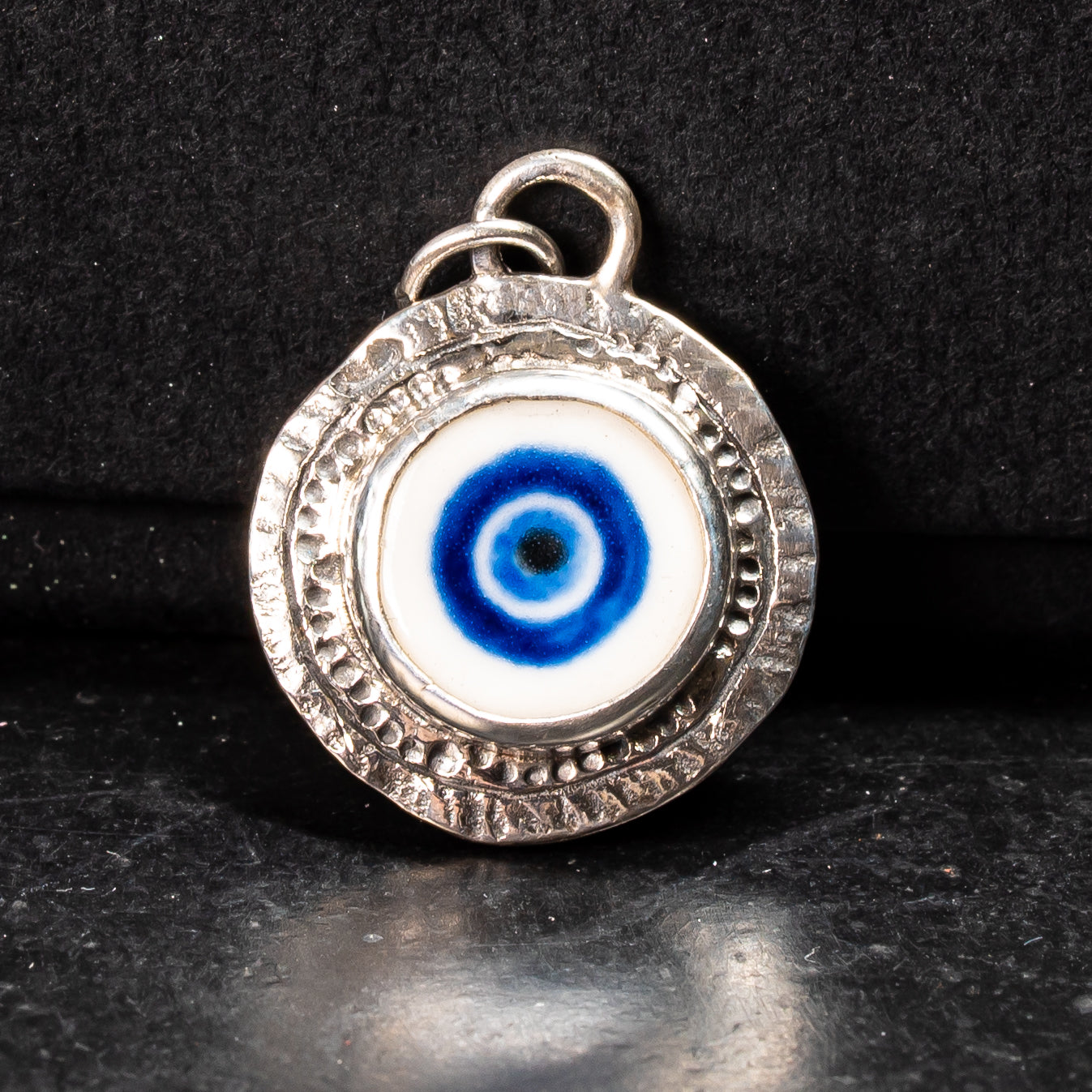 porcelain handprinted evil eye motif set in a sterling silver handmade coin pendant on a black background