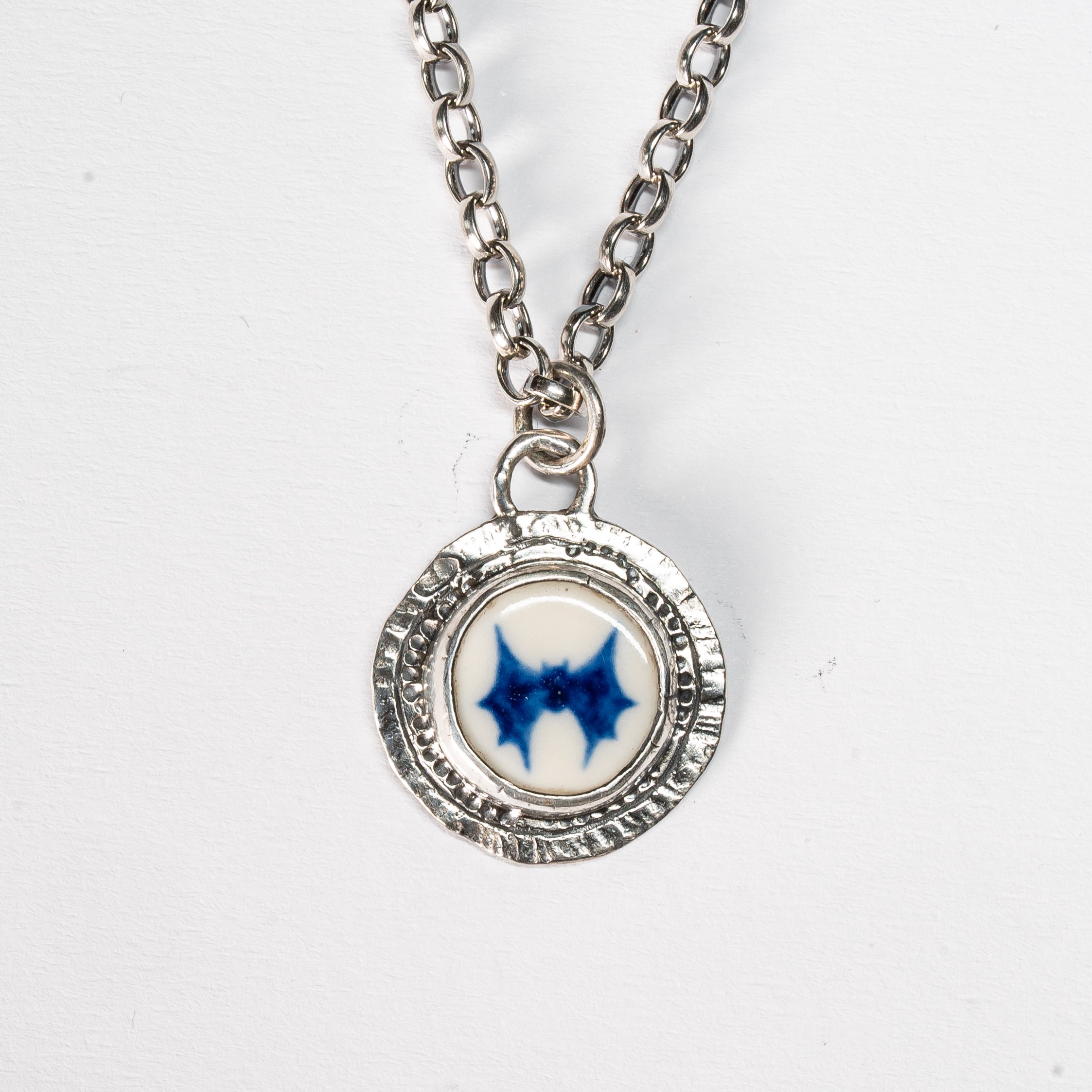 blue handprinted bat on a porcelain stone encased in a sterling silver handmade coin necklace on a white background 