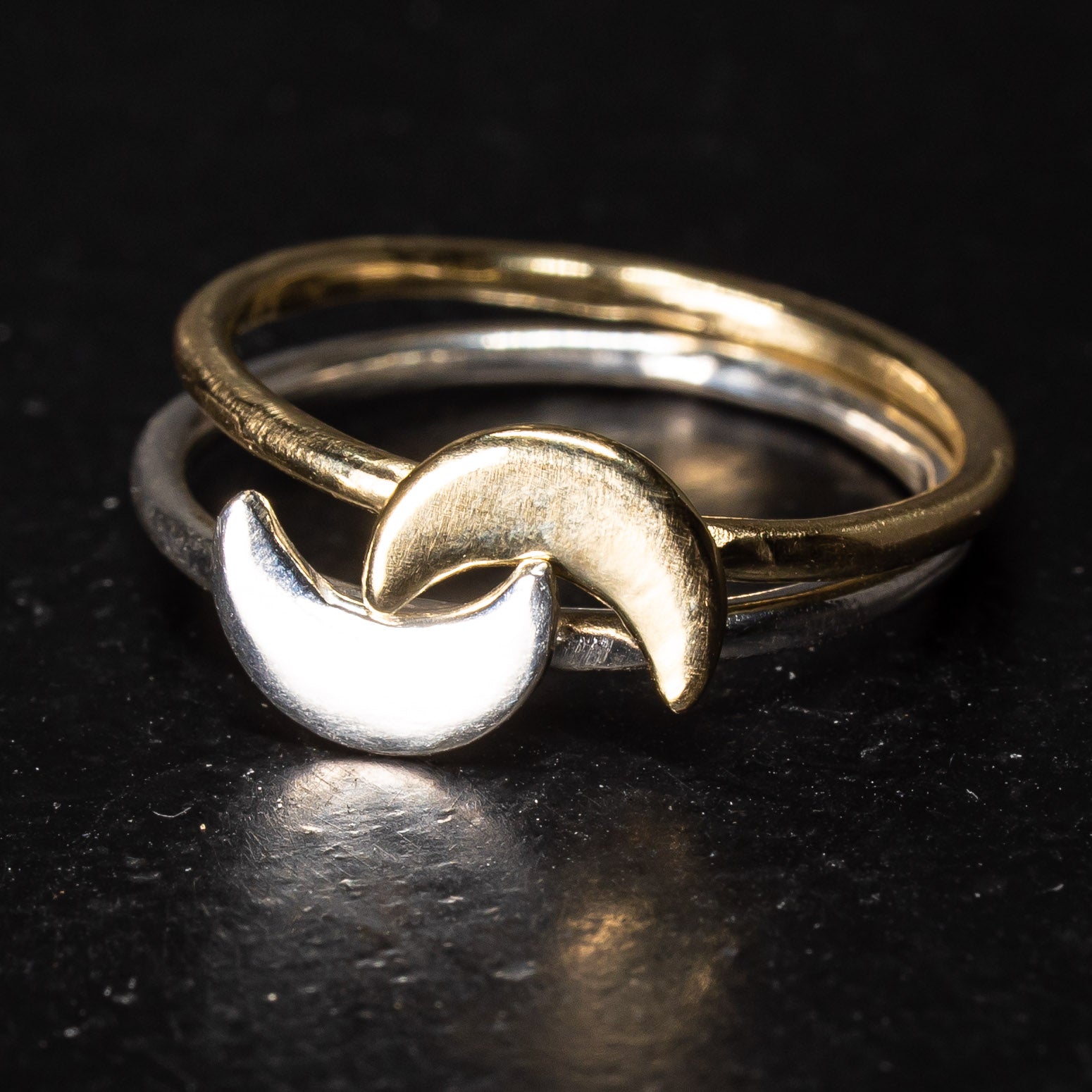 Two crescent moon rings stacked on each other one in gold and one in silver
